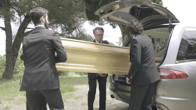 Pallbearers in hearse arriving with coffin at graveyard
