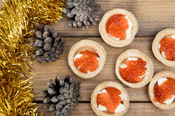 the Several tartlets with red caviar and butter tinsel fir coneson wooden brown table top view