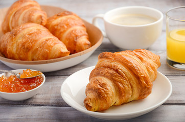 Fresh Croissants with coffee, jam and orange juice for breakfast on rustic wooden background, selective focus