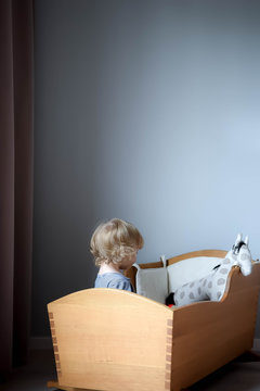 Girl playing in vintage wooden cradle at home