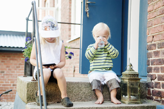 Girl and small boy sitting on step in front of house