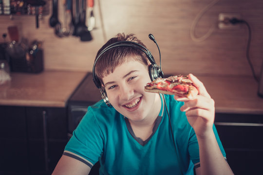 Teenager eating pizza sitting at a laptop.