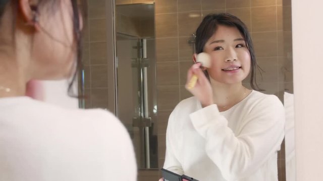 Beautiful japanese women putting on make up in mirror 