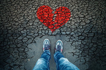 Lonely man standing on cracked asphalt floor with illustrated cracked broken heart symbol. Point of...