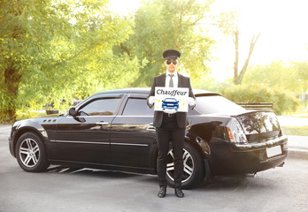Young man standing with banner CHAUFFEUR near luxury car outdoor