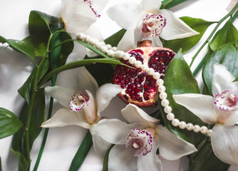 White orchids with pink spots, ripe pomegranate and pearl beads