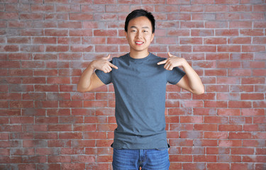 Asian man in blank grey t-shirt standing against brick wall