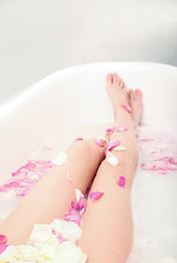 Woman relaxing in bath with foam and petals, closeup of female legs