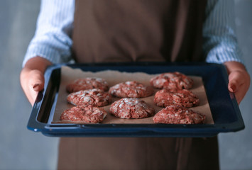 Closeup of woman holding baking tray with delicious cookies on grunge background