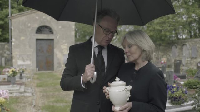 Mourners standing at funeral with cremation urn