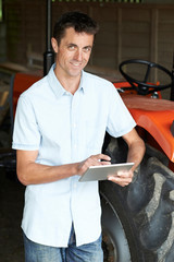 Farmer Standing Next To Tractor Using Digital Tablet