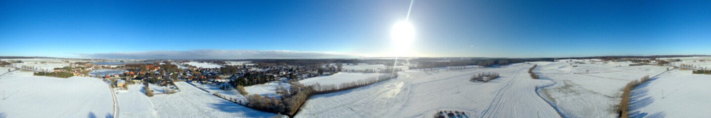 
aerial view panorama of beautiful blue sky snowy landscape with a small village and lakes  in germany