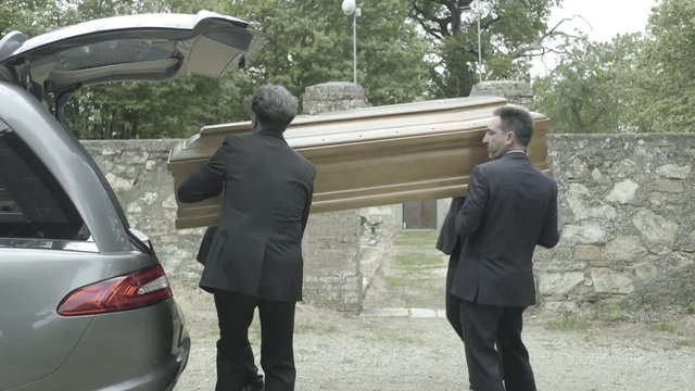 Pallbearers in hearse arriving with coffin at graveyard