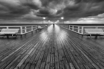 Calm Baltic Sea with illuminated pier and impressive stormy clouds on the sky. Early morning in Gdynia Orlowo. Poland. Europe- black and white