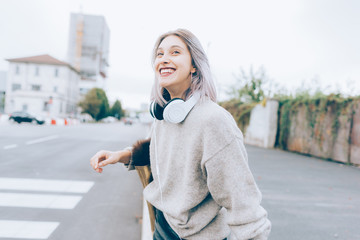 Young beautiful caucasian purple grey hair woman outdoor in the city walking listening music with head phones and smart phone hand hold - technology, relaxing, music concept