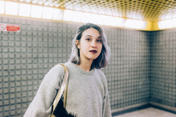 Young beautiful caucasian purple grey hair woman in the subway, looking at camera, pensive - commuter, transport, serious concept