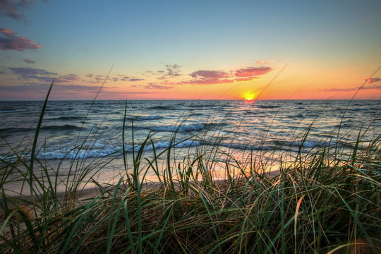Scenic Summer Sunset Background.  Beautiful sunset horizon over water with a sandy beach and dune grass in the foreground. Hoffmaster State Park. Muskegon, Michigan.