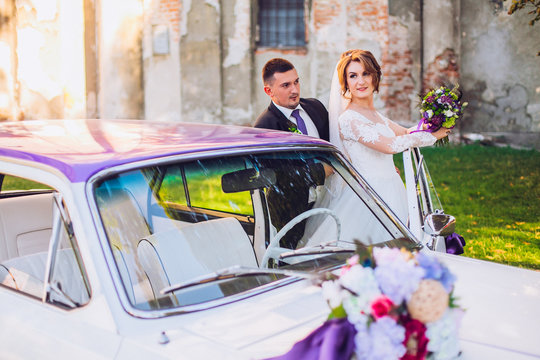 bride and groom  stay near old white and violet retro car. Newlyweds embracing.
