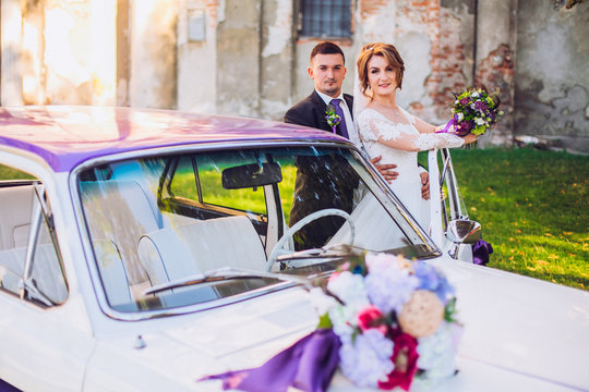 bride and groom  stay near old white and violet retro car. Newlyweds embracing.