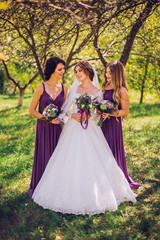Fototapeta premium Bride with bridesmaids outdoors in sunny green garden on the wedding day