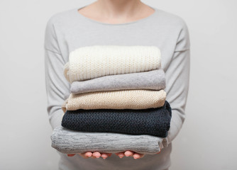 Woman holding stack of sweaters on grey background