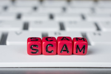 Scam word on the white keyboard showing swindles and fraud