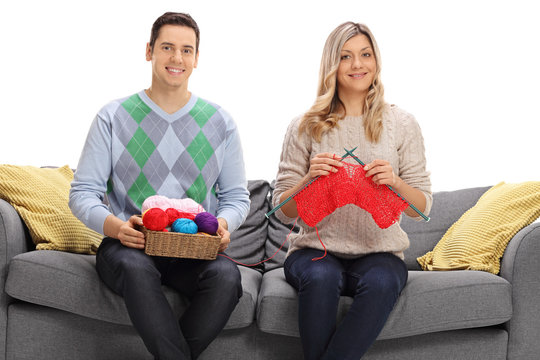 Young man sitting on sofa and helping young woman knit