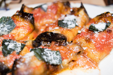 Fette di melenzana arrotolate, farcite con prosciutto e formaggio, condite con pomodoro basilico e parmigiano grattugiato e cotte al forno 