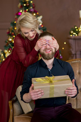 Obraz na płótnie Canvas christmas couple, happy young female surprise man cover his eyes