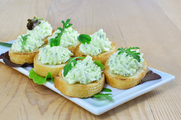 Herded cream cheese with arugula canapes on white plate