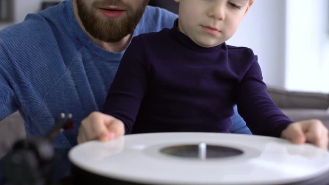 Happy bearded father listening music on vinyl records with his little cute son at home