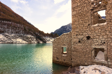 Alpine lake with ruins of old houses partially submerged by water