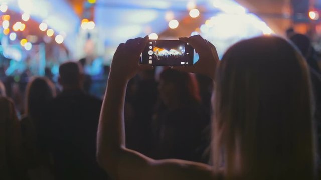 Young woman recording video of music concert on smartphone