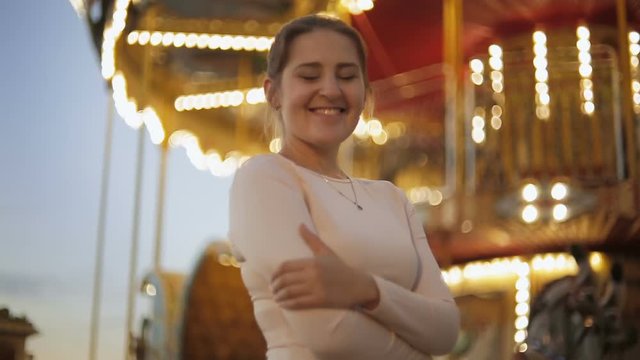 Portrait of beautiful smiling woman standing at illuminated carousel in amusement park
