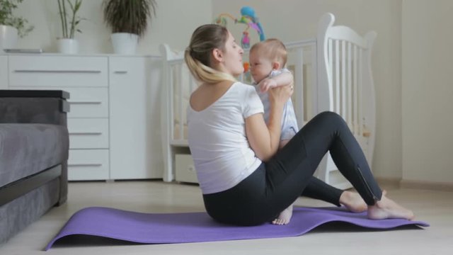 Beautfiul young woman exercising on fitness mat holding her cute baby son