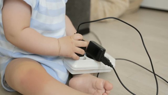 Closeup shot of little baby boy playing with charging wires and extension cable at home