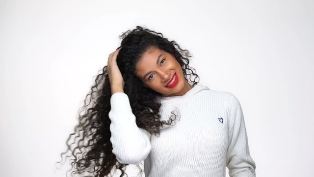 Happy African woman in white sweater posing in studio and playing with her hair