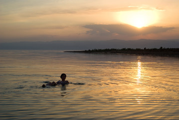 Naklejka na ściany i meble Woman floating in the Dead Sea at sunset