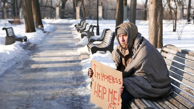 
4K.Homeless young man with cardboard  sit  and ask help in  winter city park. 
