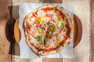 Seafood topped pizza served on plate with wooden background.