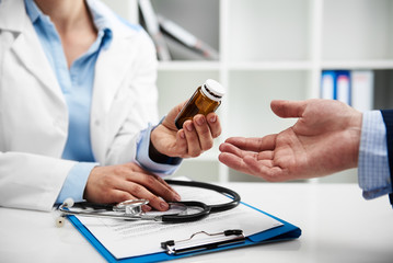 Female doctor giving pills bottle to male patient in clinic. Concept of healthcare, medical treatment and insurance. - 133646819