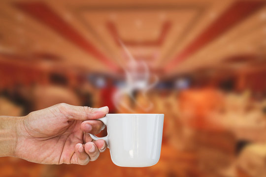 Hand holding hot coffee cup on blurred hotel lobby background