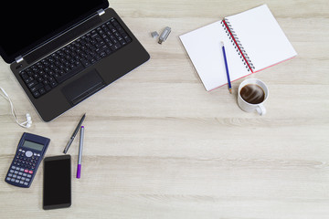 Computer laptop with mobile phone, office supplies and hot black coffee cup with steam on vintage wooden desk background view from above, business concept
