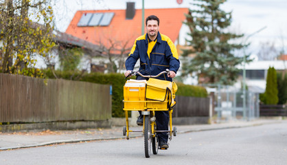 Briefträger fährt auf seinem Lastenfahrrad Post in Wohngebiet aus 