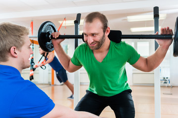 Mann stemmt Gewichte im Fitness-Center unter Anleitung von Personal Trainer