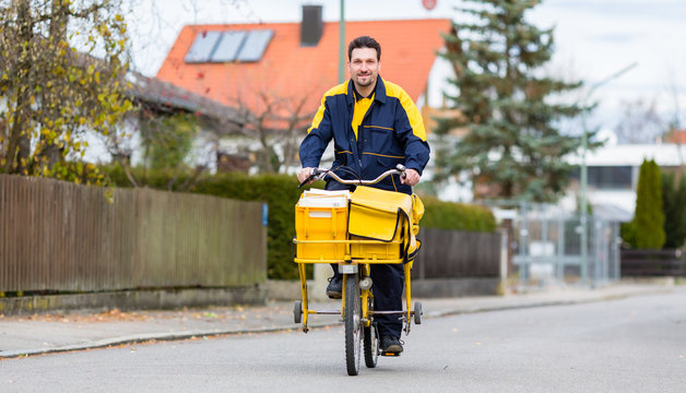 Brieftr&auml;ger f&auml;hrt auf seinem Lastenfahrrad Post in Wohngebiet aus 