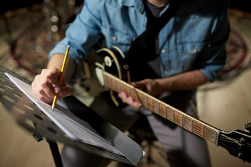 man with guitar writing to music book at studio