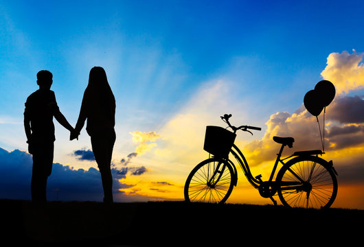 Silhouette of sweet couple in love happy time and bicycle in bea