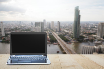 Computer laptop on wooden table top on blurred city background top view