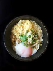Top view bowl of japanese food, noodles with egg onsen in black bowl background.
